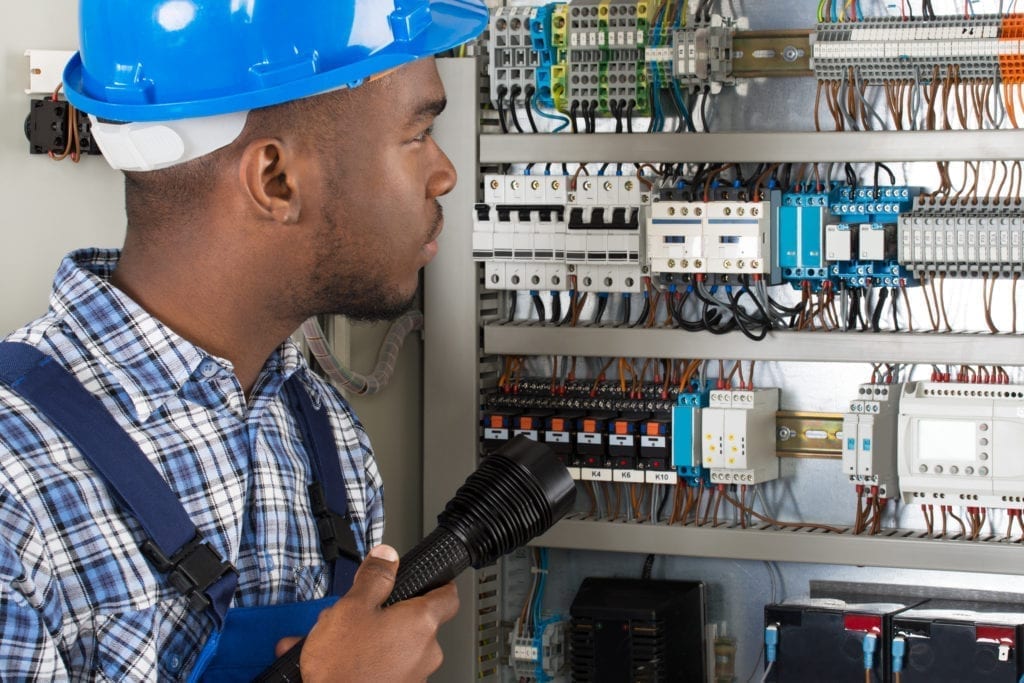 Young African Male Technician Analyzing Fusebox With Flashlight