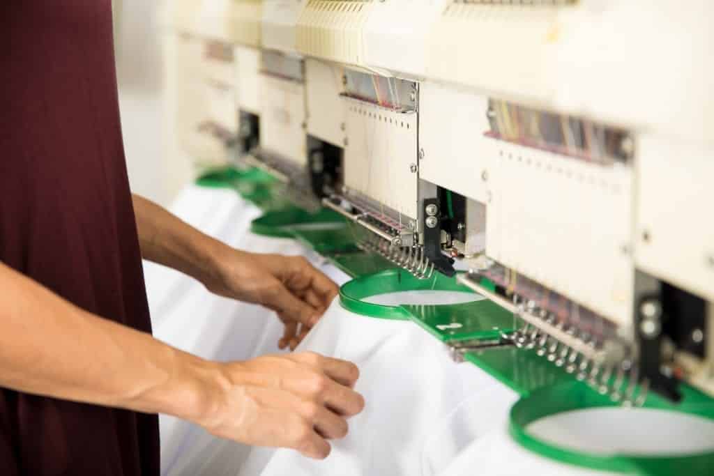 Closeup of a woman placing several garments on an embroidery machine in a textile factory