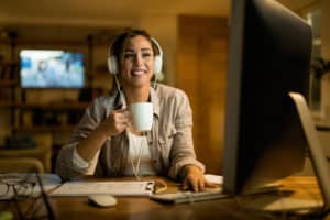 A woman with headphones is drinking some coffee while doing her final tasks for the night
